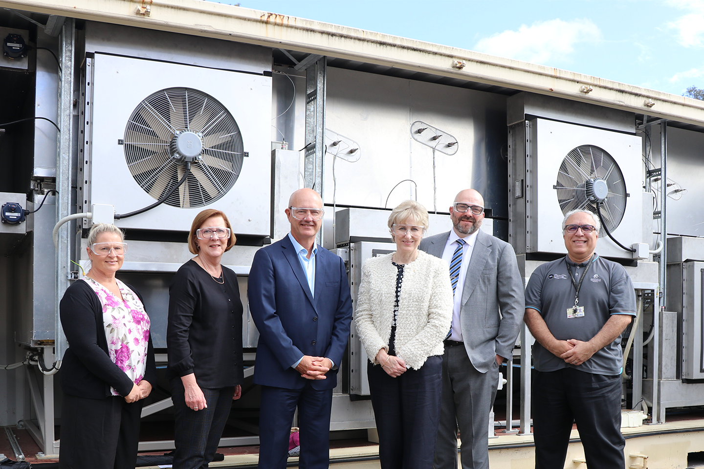 Six people stood in front of, an industrial sized wall of fans, all smiling. 